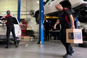 Mechanic carrying box with coworker working on car in background at Autofix Service Centre in Adelaide